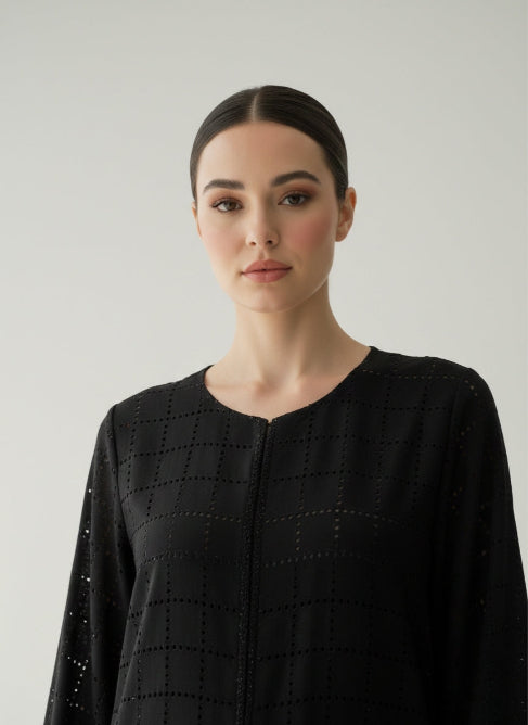 Woman wearing a black lasercut Abaya from CAS Abaya with intricate patterns against a plain background
